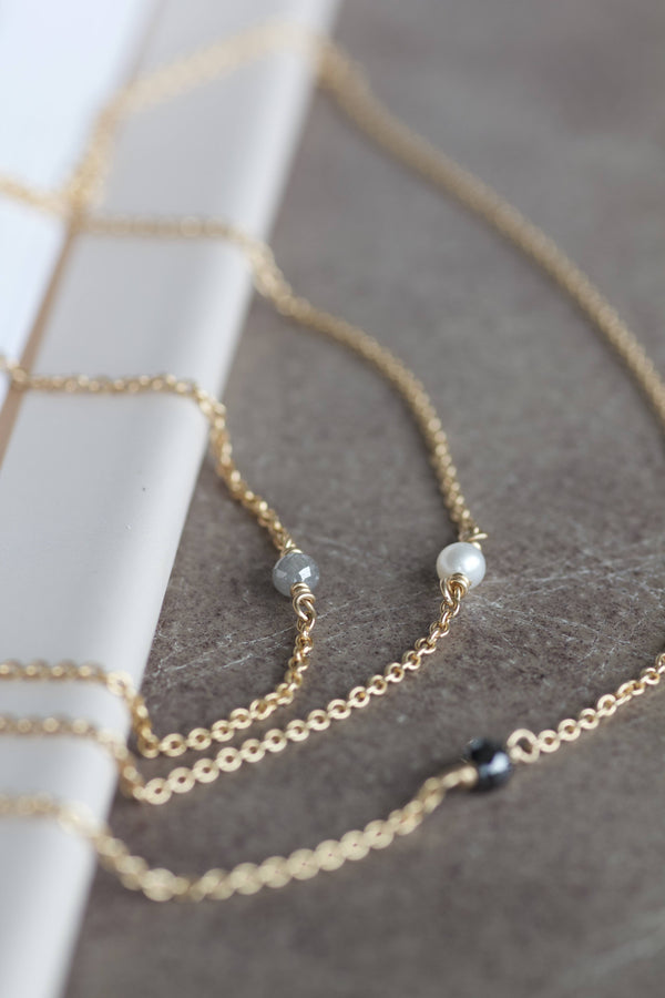 Alaia halskæder i 14 karat guld og med enkel, sort diamant, hvid perle eller grå diamant. Kæden er en rund ankerkæde.  POMPUS smykker er håndlavet og fra eget værksted her i Danmark