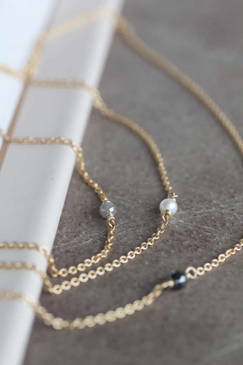 Alaia halskæder i 14 karat guld og med enkel, sort diamant, hvid perle eller grå diamant. Kæden er en rund ankerkæde.  POMPUS smykker er håndlavet og fra eget værksted her i Danmark