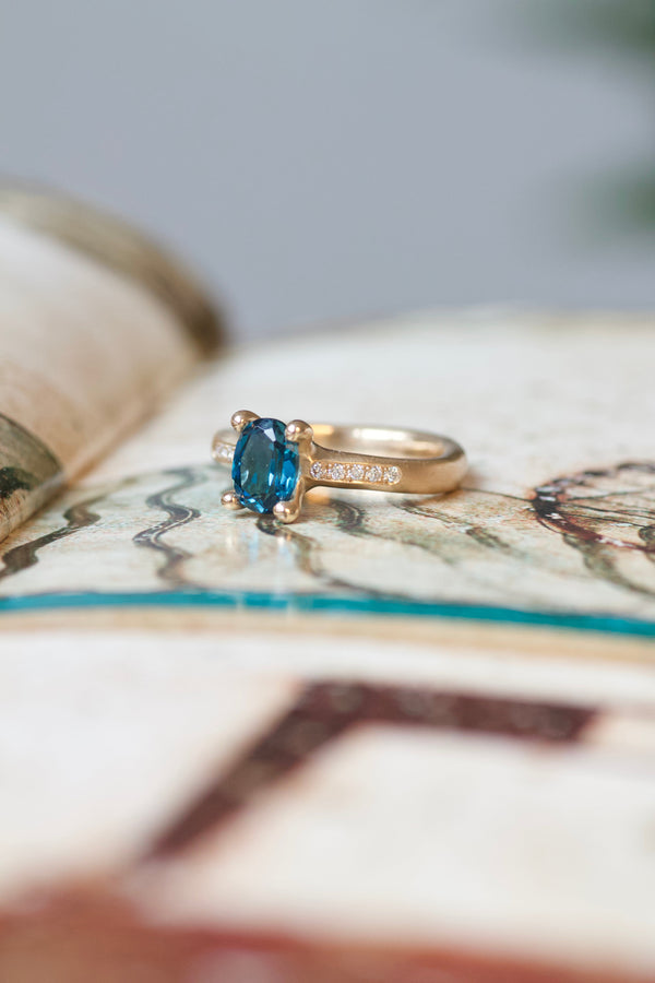 Lækker guldring i matteret, rustikt design.All about ringene skal male verden i farver og symboliserer alt, der giver værdi for den, der bærer den. Mens de emmer af farver og liv, gemmer de på et tomt lærred, der venter på sin historie og betydning. Hvad skal de symbolisere for dig?  Fatted med en oval, facetteret london blue topas samt brillanter ned af siderne.